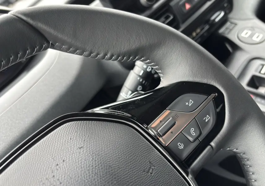 Gros plan sur le volant cuir multifonctions du Peugeot Rifter gris artense, mettant en valeur les commandes audio et téléphone.