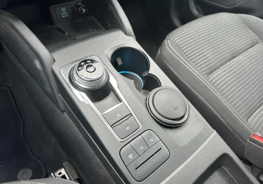 Gros plan sur la console centrale noire du Ford Kuga 2020 avec sélecteur rotatif de vitesse et porte-gobelets.