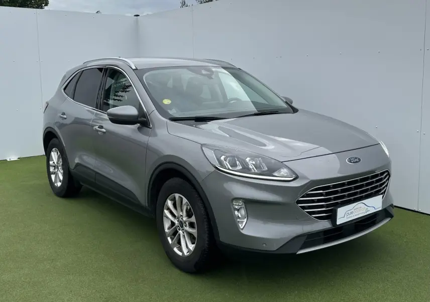 Ford Kuga gris solaire en 3/4 avant droit avec barres de toit aluminium et jantes alliage 17 pouces.