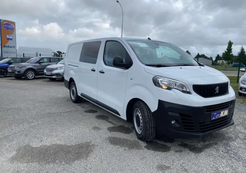 Peugeot Expert Fourgon blanc vu en 3/4 avant droit sur parking avec calandre noire et feux allumés.