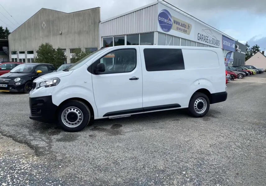 Peugeot Expert Fourgon blanc vu de profil côté gauche, stationné devant un garage avec porte coulissante.