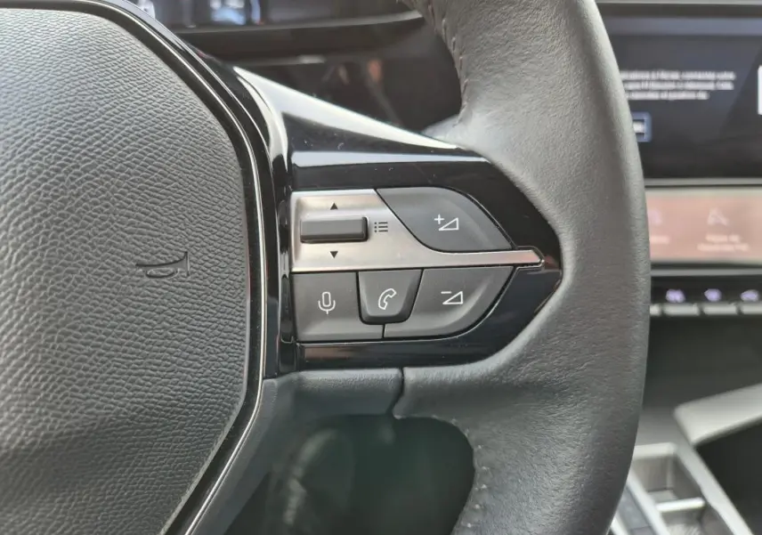 Gros plan sur les commandes au volant à droite du Peugeot 308 2024, intérieur noir avec affichage numérique en arrière-plan.