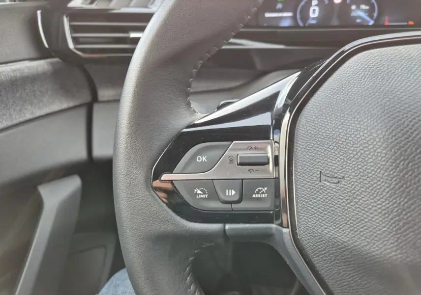 Gros plan sur le volant noir de la Peugeot 308 2024 avec commandes intégrées et tableau de bord numérique en arrière-plan.