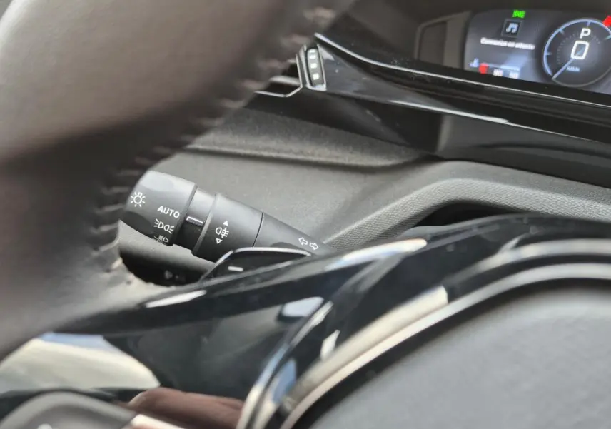 Vue rapprochée du volant et du commodo gauche de la Peugeot 308 2024, avec affichage numérique en arrière-plan.