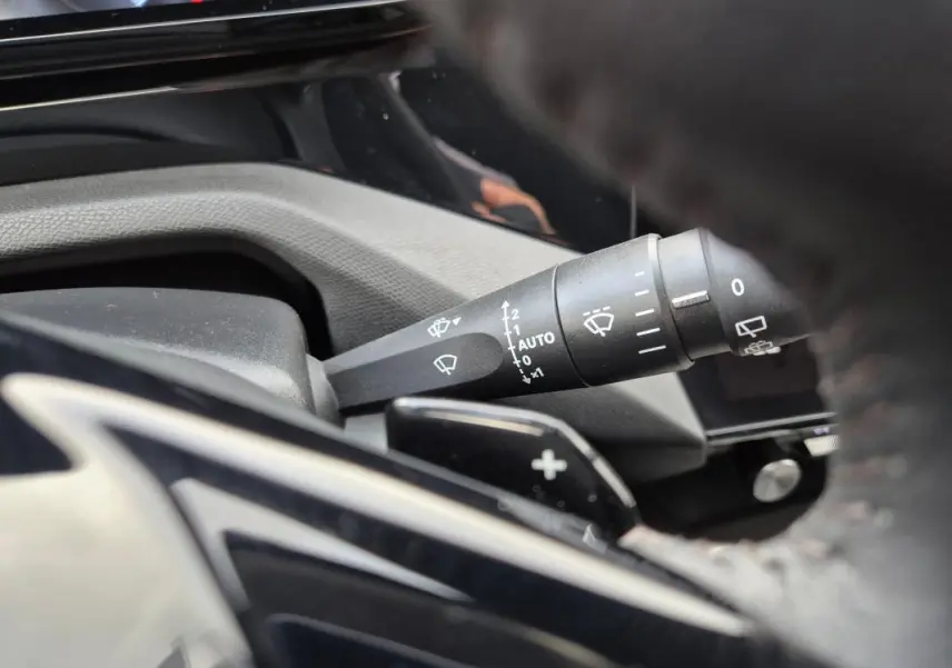 Gros plan sur la commande des essuie-glaces côté gauche du volant dans l’habitacle d’une Peugeot 308 bleu 2024.