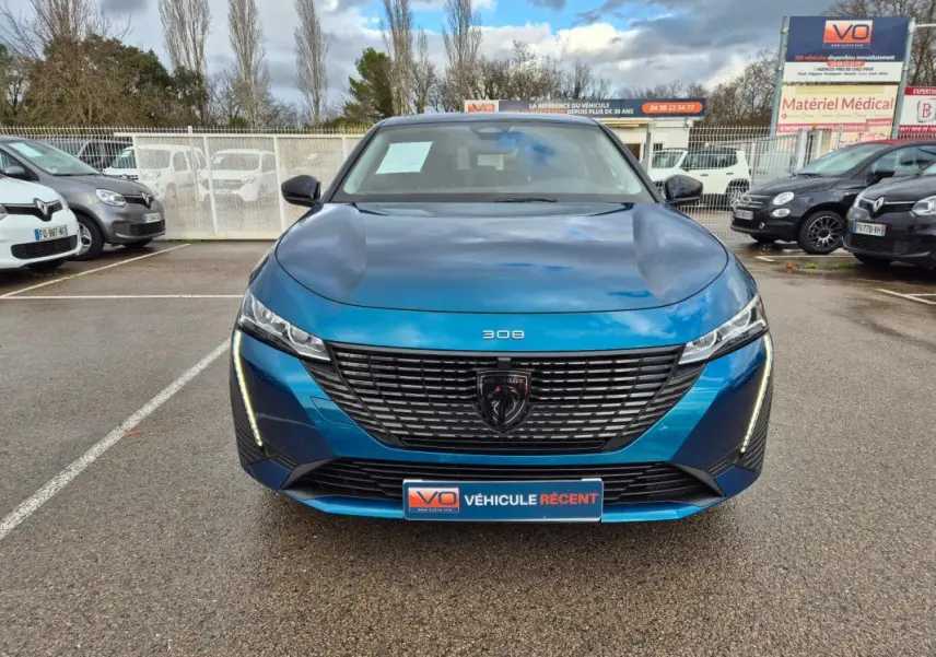 Vue frontale d'une Peugeot 308 bleu métallisé 2024 avec calandre noire et feux LED verticaux allumés.