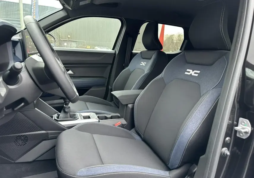 Vue intérieure côté conducteur du Dacia Duster noir 2025, sièges avant bi-matière avec logo DC brodé.