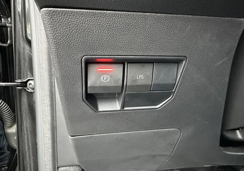 Gros plan sur les commandes du frein de stationnement électrique et du bouton GPL, tableau de bord noir du Dacia Duster 2025.