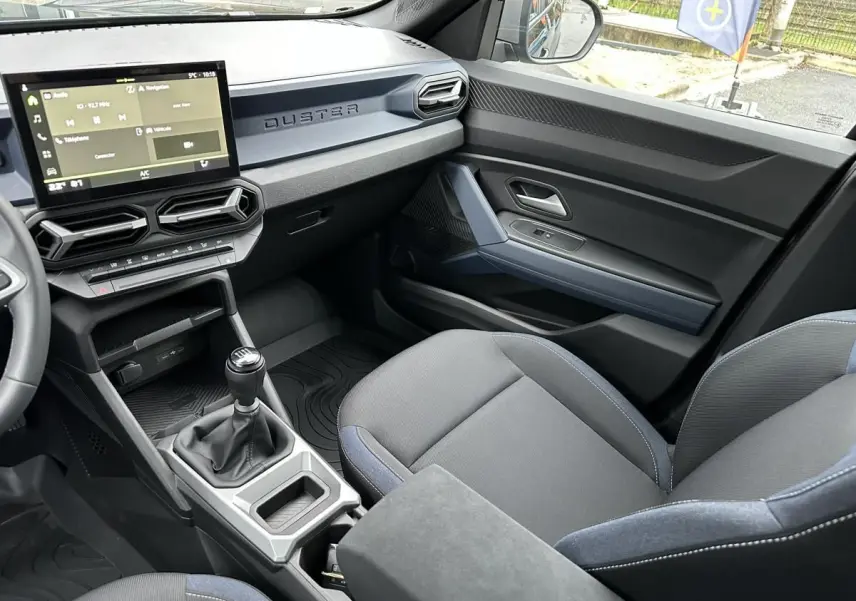 Intérieur du Dacia Duster 2025 vu côté passager, montrant la console centrale avec boîte manuelle et sièges noirs.