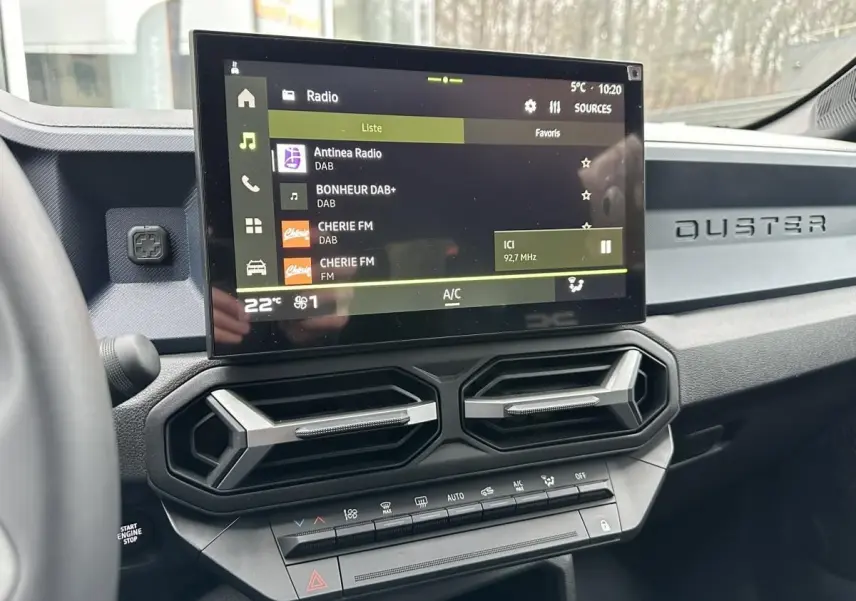 Vue intérieure centrée sur la console centrale du Dacia Duster 2025 avec écran tactile et aérateurs hexagonaux.