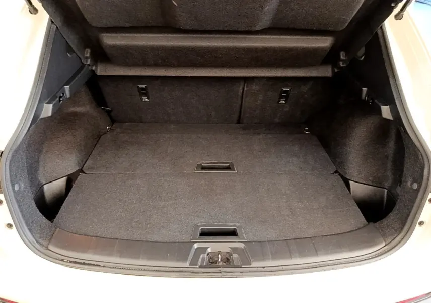 Coffre ouvert vu de face d’un Nissan Qashqai blanc, montrant l’espace de chargement avec banquette rabattue.