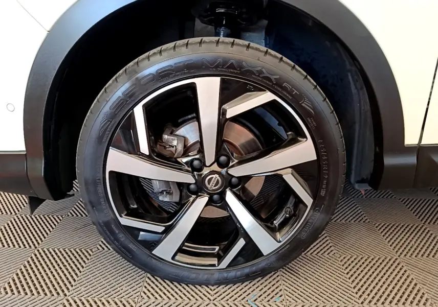 Gros plan sur la roue avant droite du Nissan Qashqai blanc, mettant en valeur la jante alliage bicolore.