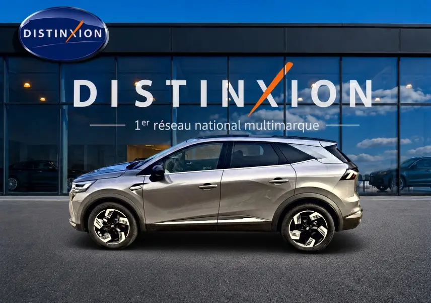 Profil droit du Renault Symbioz gris cassiopée 2026, SUV hybride avec jantes alu et vitres surteintées, devant une vitrine Distinxion.
