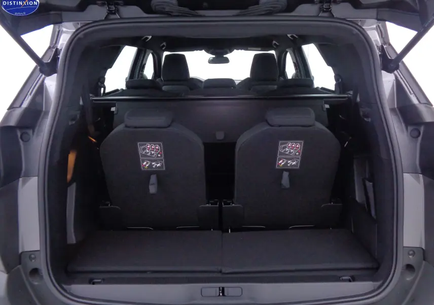 Vue arrière du coffre ouvert d'un Peugeot 5008 gris platinium, montrant les sièges arrière relevés et l'intérieur noir.