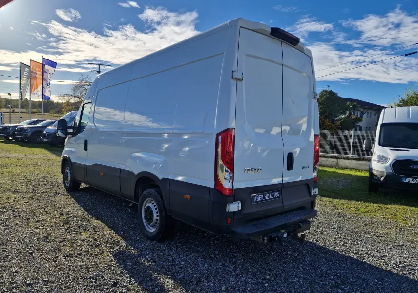 Fourgon Iveco Daily blanc vu en 3/4 arrière droit, avec marchepied arrière et attelage visible, stationné en extérieur.