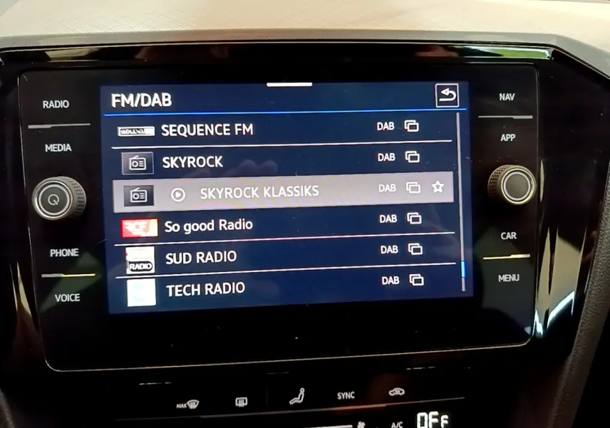 Écran tactile central affichant les stations radio numériques dans l'habitacle d'une Volkswagen Passat gris foncé.