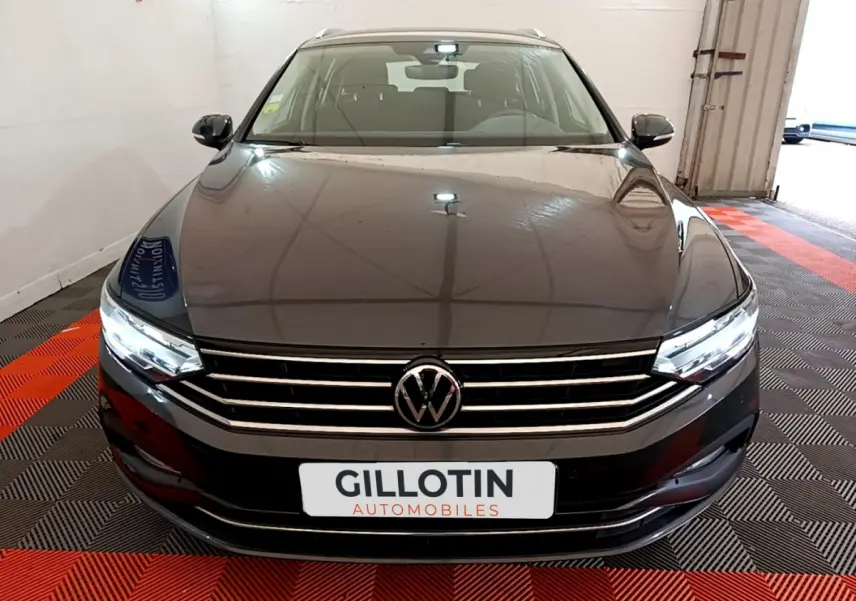 Vue frontale d'une Volkswagen Passat gris foncé 2021 avec calandre chromée et phares LED allumés dans un showroom.