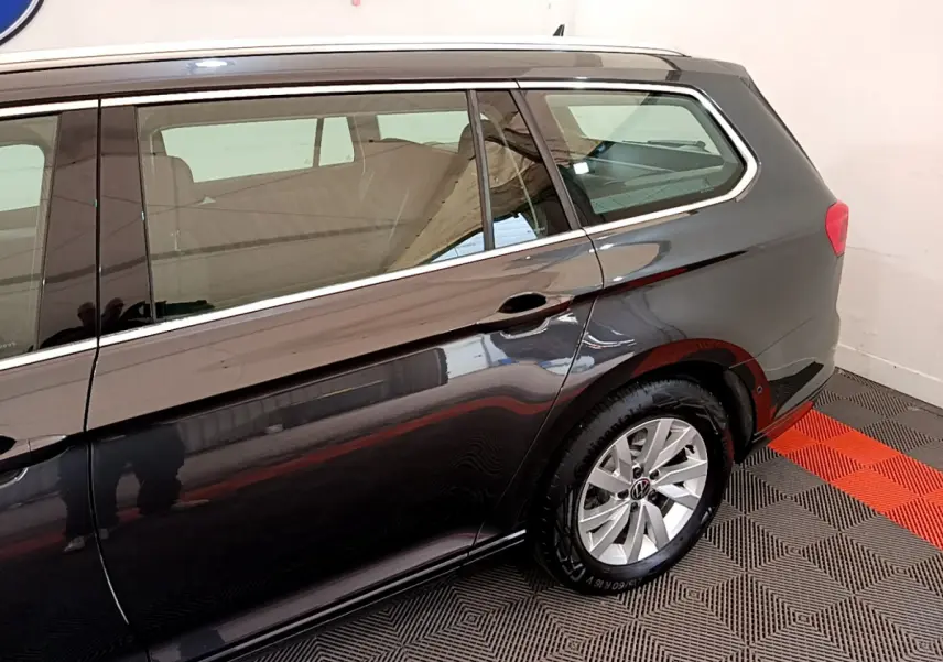 Vue latérale côté droit d'une Volkswagen Passat gris foncé break, mettant en valeur la roue arrière et les vitres teintées.