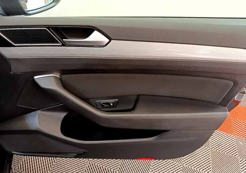 Gros plan sur la porte intérieure côté conducteur d'une Volkswagen Passat gris foncé, avec poignée et commande de verrouillage.