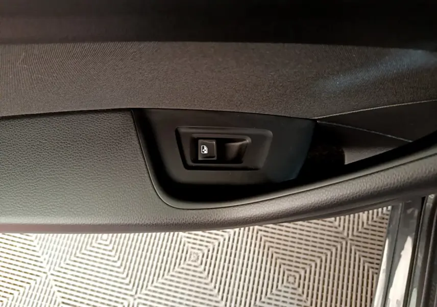 Bouton de déverrouillage électrique de la porte intérieure, sur panneau noir texturé côté conducteur d'une Volkswagen Passat gris foncé.