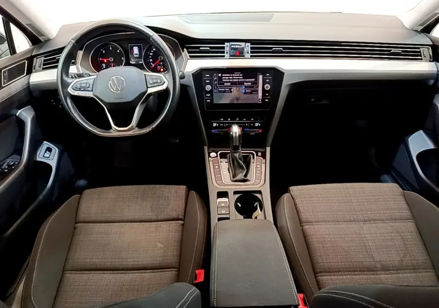 Intérieur avant de la Volkswagen Passat 2021, vue du tableau de bord avec volant cuir et sièges tissu marron.