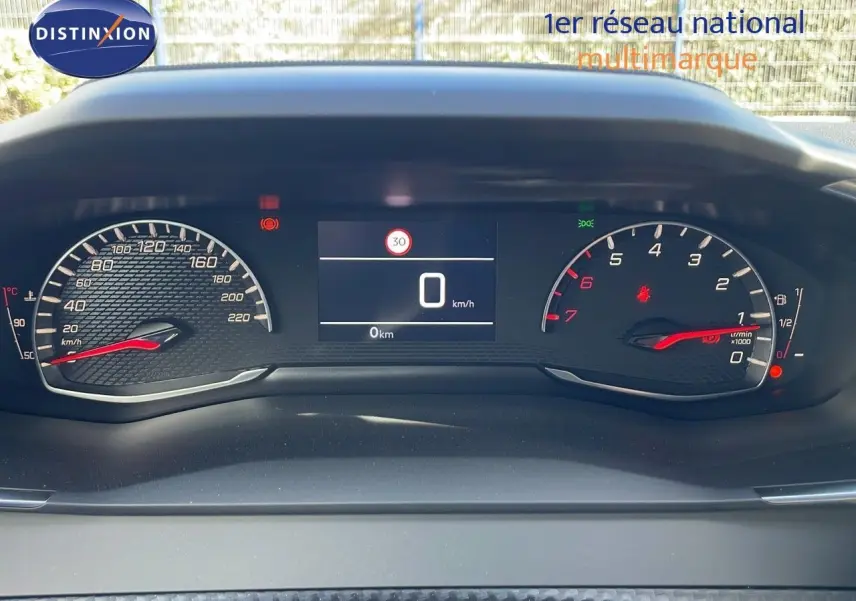 Tableau de bord numérique du Peugeot 2008 blanc, affichant vitesse à 0 km/h et compte-tours au ralenti.