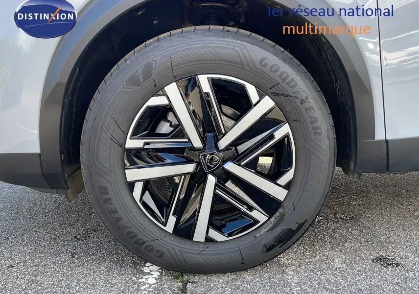 Gros plan sur la roue avant gauche d'un Peugeot 2008 blanc Okenite avec jante alliage bicolore moderne.