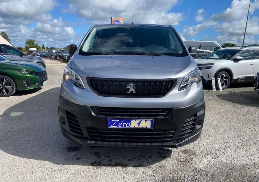 Vue frontale d'un Peugeot Expert Fourgon gris Artense métallisé avec calandre noire et plaque "Zéro KM" visible.