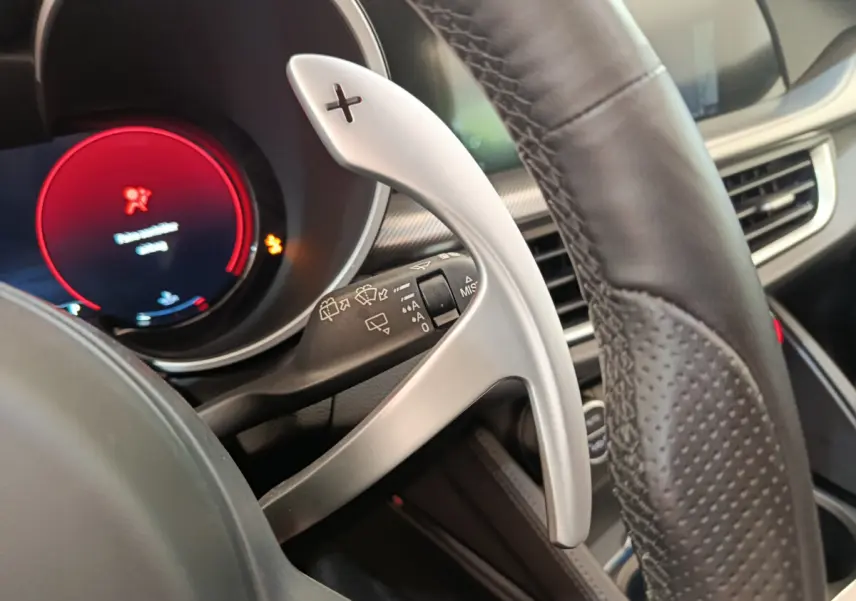 Gros plan sur la palette de changement de vitesse alu et cuir du volant de l'Alfa Romeo Stelvio gris foncé 2024.