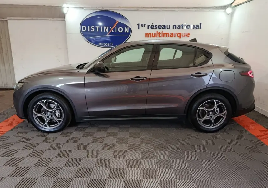 Profil côté gauche d'un Alfa Romeo Stelvio gris foncé 2024 Sprint, avec jantes distinctives et feux arrière LED allumés.