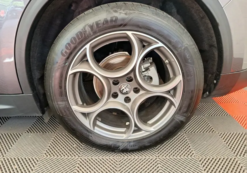 Gros plan sur la roue arrière droite d'un Alfa Romeo Stelvio gris foncé, montrant le passage de roue et le pneu.