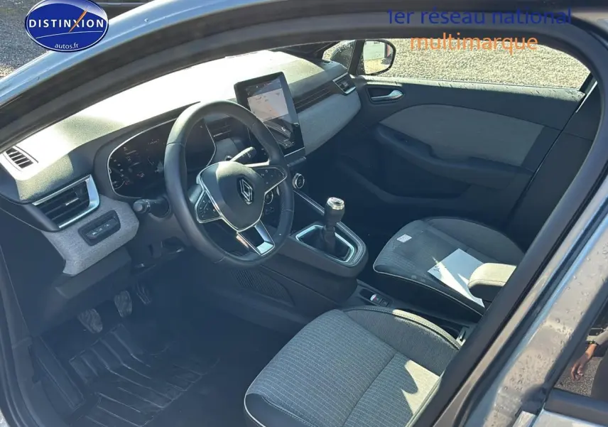 Intérieur avant droit d'une Renault Clio V gris pizzara, volant textile, boîte manuelle et écran tactile central visible.