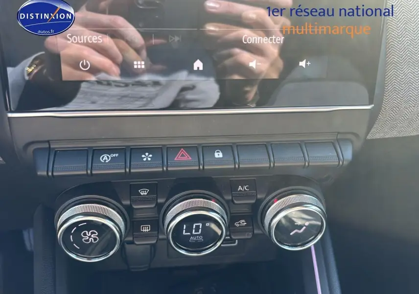 Gros plan sur la console centrale de la Renault Clio V gris pizzara, montrant les commandes de climatisation et les boutons fonctionnels.