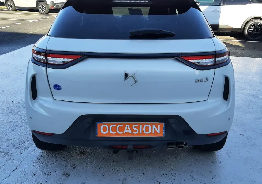 Vue arrière d'une DS3 Crossback blanc perle avec toit noir, plaque orange "OCCASION" visible sur un parking.