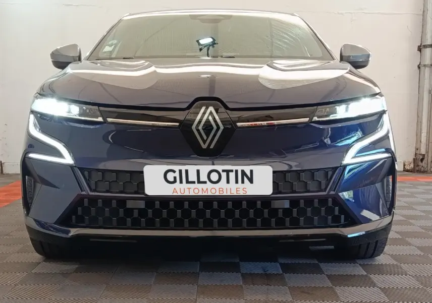 Vue frontale d'une Renault Mégane Techno EV60 bleu avec feux LED allumés et calandre noire à motifs géométriques.
