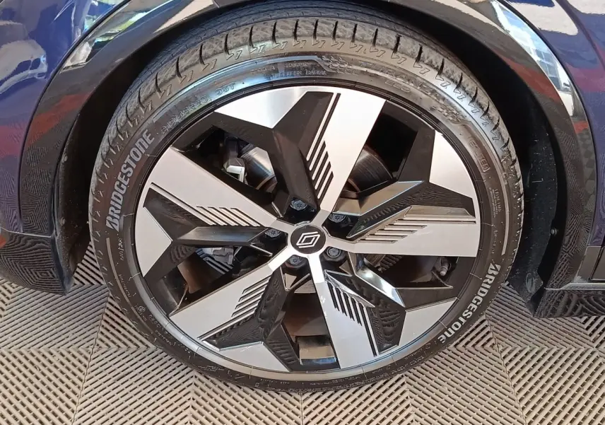Gros plan sur la roue avant droite de la Renault Mégane Techno EV60 bleu, jante alliage design noir et argent.