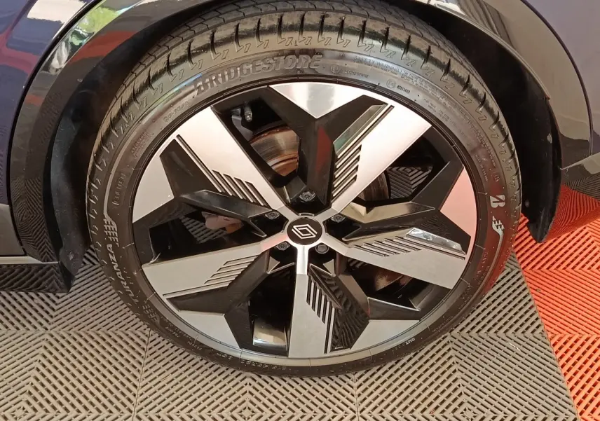 Gros plan sur la roue avant gauche de la Renault Megane Techno EV60 bleu, jante alliage noire et argentée au design géométrique.