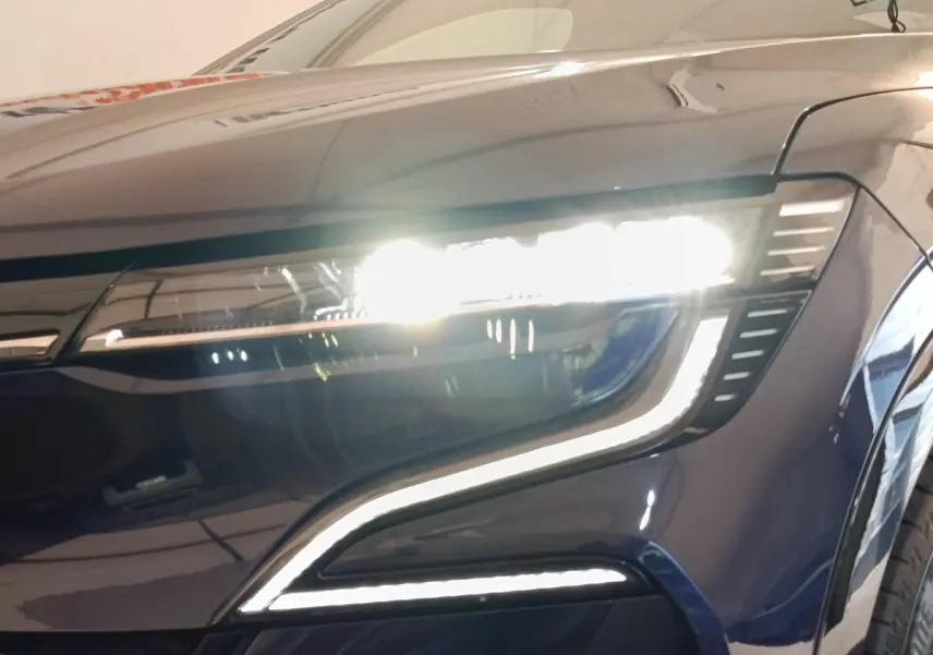 Gros plan sur le phare avant droit allumé de la Renault Mégane Techno EV60 bleu électrique 2023.
