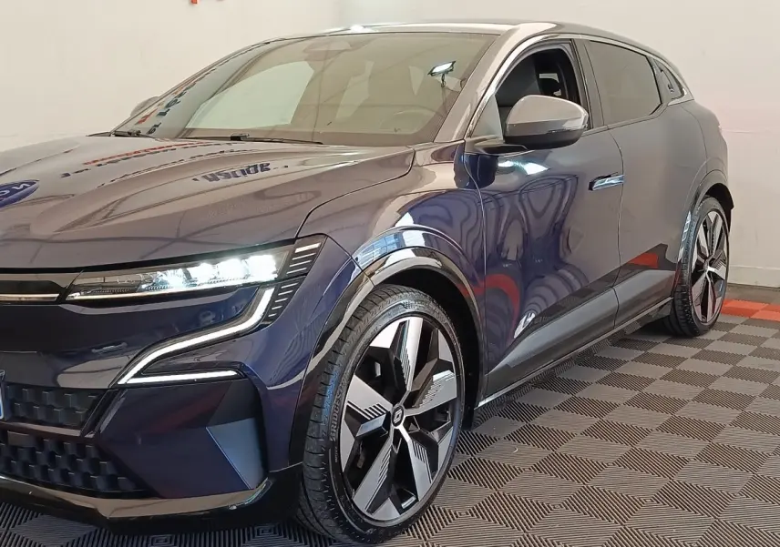 Vue 3/4 avant droit d'une Renault Mégane Techno EV60 bleu électrique avec phares LED allumés et jantes stylisées.