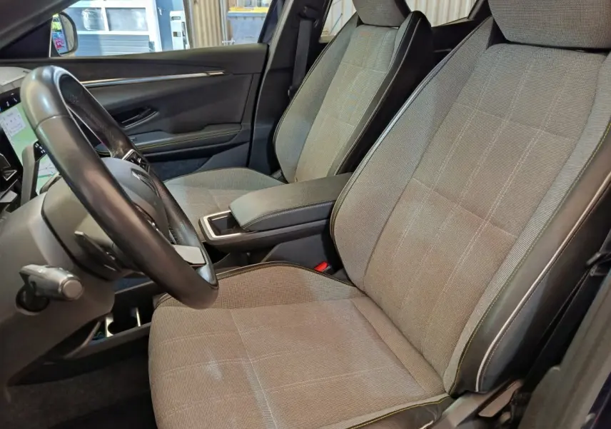 Vue intérieure côté conducteur de la Renault Megane Techno EV60 2023, sièges tissu gris clair avec surpiqûres contrastées.