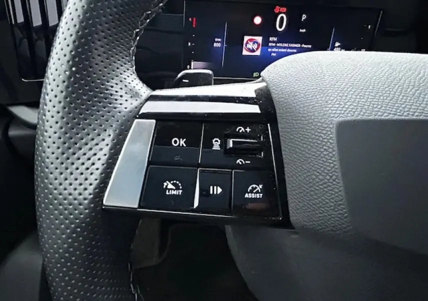 Gros plan sur les commandes gauche du volant cuir perforé de l'Opel Astra VI Diesel 2022 avec affichage numérique.