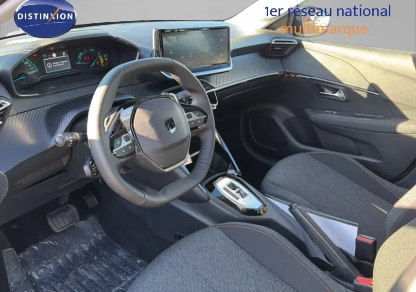 Intérieur avant droit de la Peugeot 208 1.2 Hybrid 2025 avec volant compact, écran tactile et sièges tissu gris.