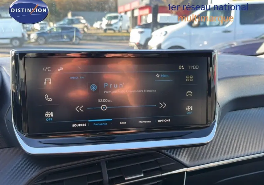 Écran tactile central allumé affichant la radio dans l'habitacle d'une Peugeot 208 gris Artense 2025.