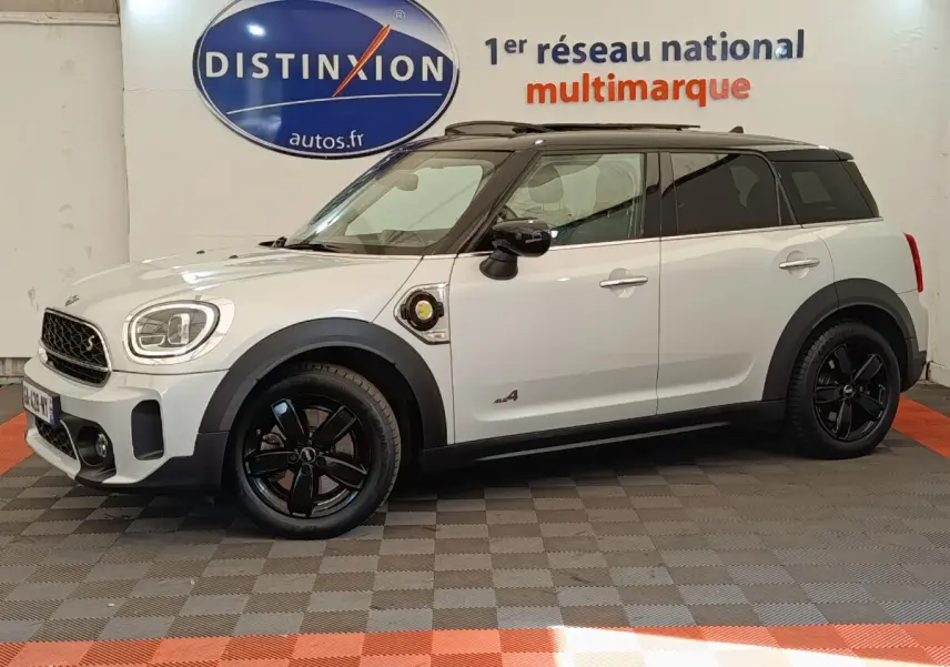 Vue latérale droite d'une MINI Countryman Cooper SE hybride blanche avec toit noir et jantes noires en intérieur showroom