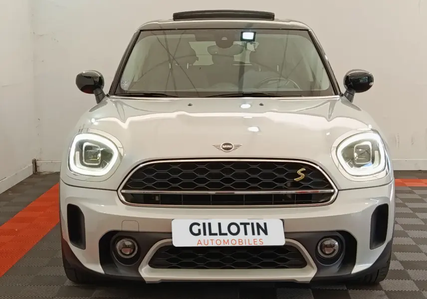 Vue frontale d'une MINI Countryman Cooper SE blanche avec phares LED allumés et calandre noire hexagonale.