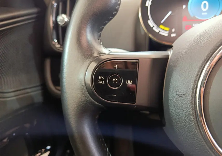 Gros plan sur les commandes de régulateur de vitesse au volant cuir noir du MINI COUNTRYMAN hybride blanc, tableau de bord en arrière-plan.