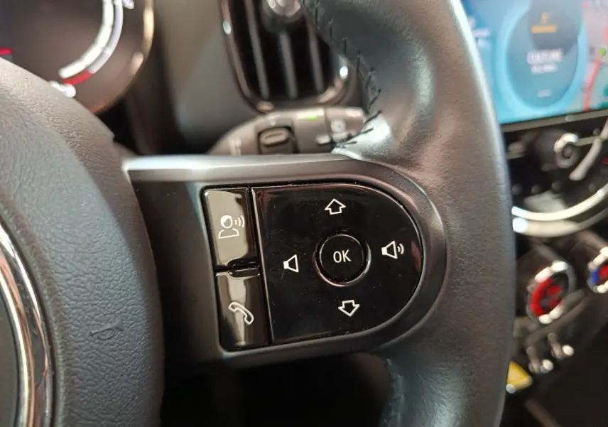Gros plan sur les commandes vocales et téléphone du volant cuir noir d'une MINI Countryman blanche, tableau de bord en arrière-plan.