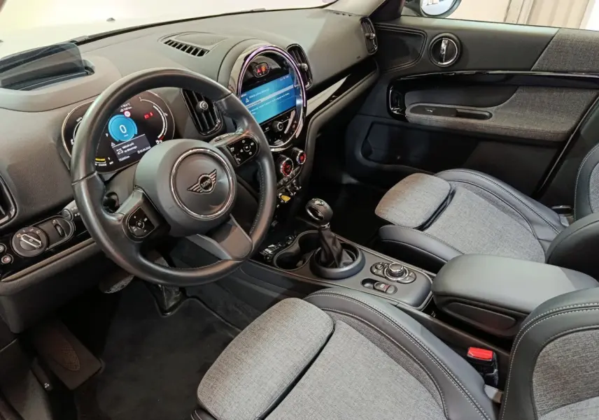 Intérieur avant droit du MINI Countryman Cooper SE, tableau de bord noir avec écran tactile circulaire et sièges tissu gris.