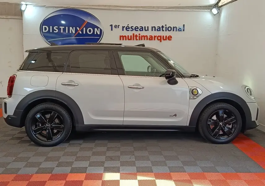 Profil droit d'un MINI Countryman Cooper SE blanc avec toit noir et jantes noires dans un showroom intérieur.