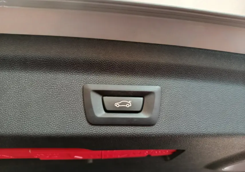 Gros plan sur le bouton d'ouverture électrique du coffre, intérieur noir texturé du hayon du MINI Countryman blanc.